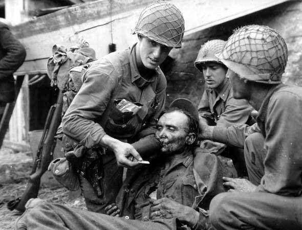 Un officier américain donne à boire à un soldat allemand blessé