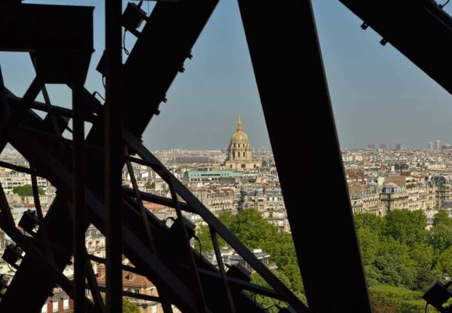 Entre les mailles de la Tour Eiffel, on devine certains monuments parisiens comme les Invalides