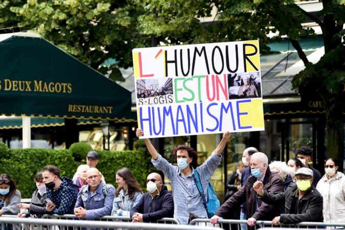 Un homme parmi les anonymes tient un panneau "L'humour est un humanisme" en hommage aux combats de Guy Bedos contre le racisme.