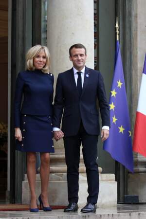 Brigitte Macron en robe courte bleue à boutons dorés et hauts talons